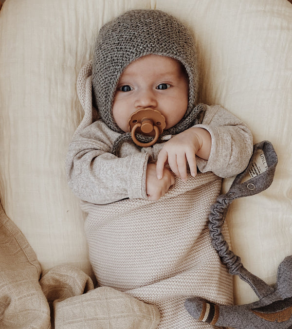 Baby mit grauer Strickmütze vor beigem Hintergrund