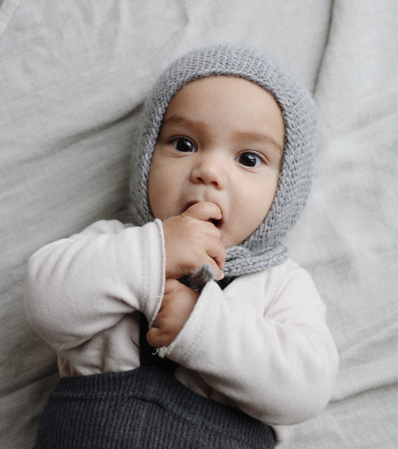 Baby mit grauer Strickmütze vor grauem Hintergrund